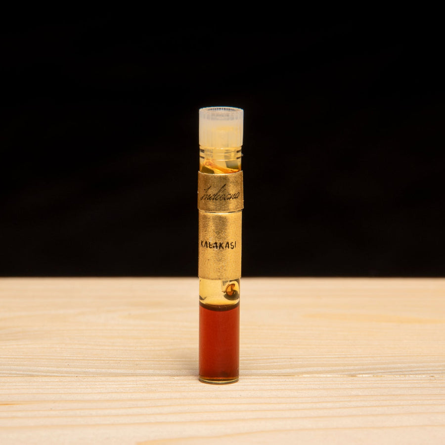 Three small glass vials with gold-colored metal collars labeled 'Indicana' and handwritten names 'KALAKASI', 'SEUFI', and 'HINDI MALiKI' on a wooden surface.
